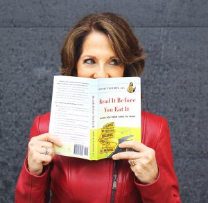 Dietitian Speaker Bonnie Taub-Dix peeks mischievously over the top of her book, "Read It Before You Eat It." She wears a red leather jacket with a zipper. 