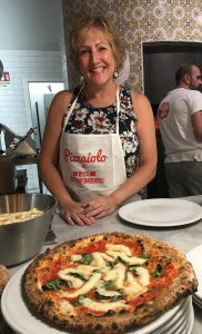 Dietitian Speaker Paula Quatromoni stands in an apron behind a pizza she crafted during an Italian cooking class.