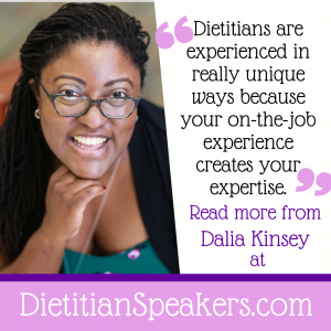 Dietitian Speaker Dalia Kinsey is ready to present, in a green shirt with black jacket, glasses, and a big smile.