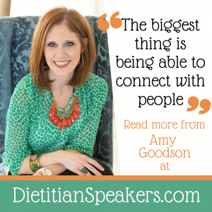 Dietitian Speaker Amy Goodson leans forward in her chair as if to share something special with her audience. She's wearing a green patterned top and a bright orange necklace, plus a big smile.